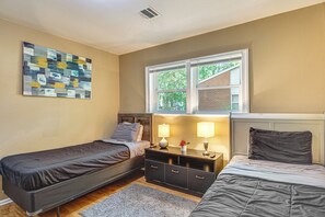 A bedroom with two single beds, a nightstand with lamps, a wall art piece, and a window with a view of trees.
