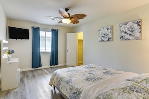 A bedroom with a bed, a ceiling fan, a TV, and a door leading to another room.