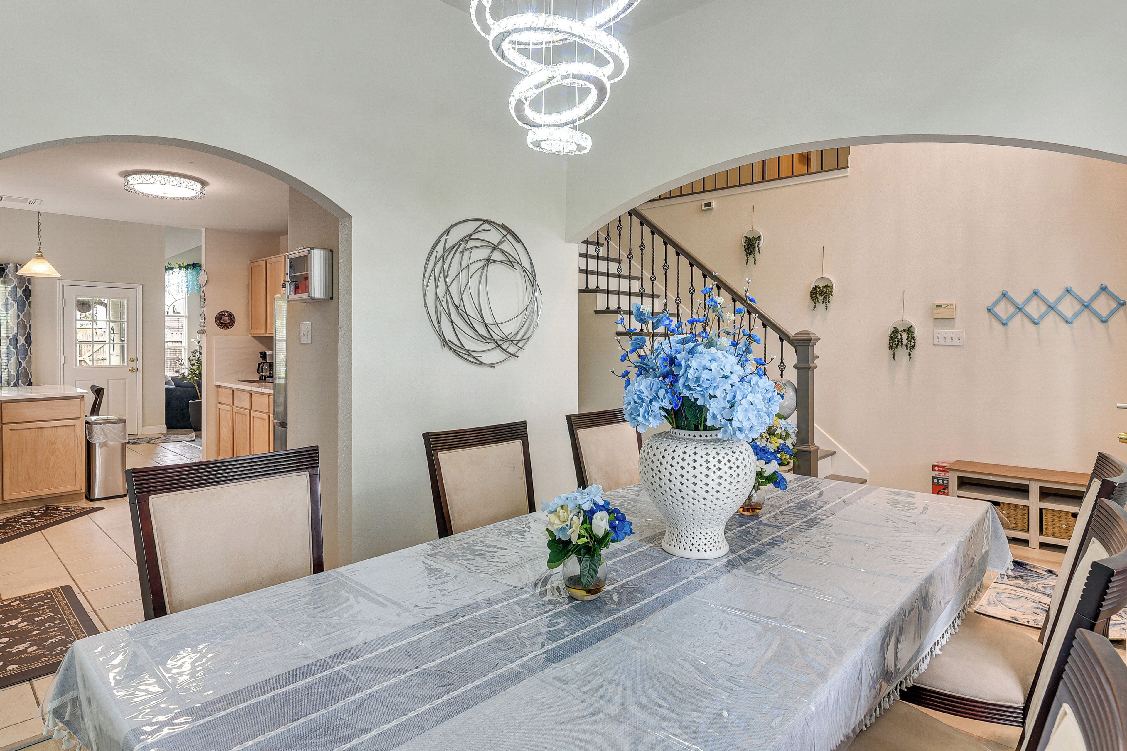 Un coin repas avec une table couverte, des chaises, un vase décoratif avec des fleurs et un escalier muni d’une rampe.