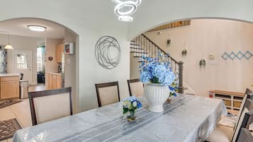 Un coin repas avec une table couverte, des chaises, un vase décoratif avec des fleurs et un escalier muni d’une rampe.