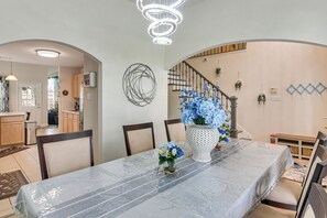 A dining area with a covered table, chairs, a decorative vase with flowers, and a staircase with a railing.