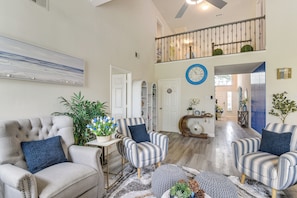 A spacious living area with a high ceiling, a staircase, and a clock on the wall.