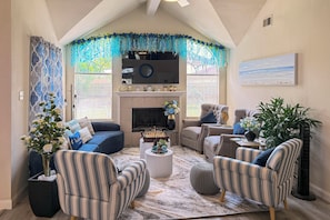 A living room with a fireplace, striped chairs, a sofa, and a large window with blinds.