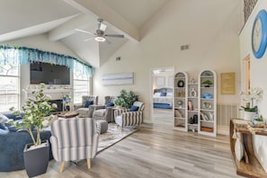 A spacious living room with a high ceiling, a fireplace, and a large window.