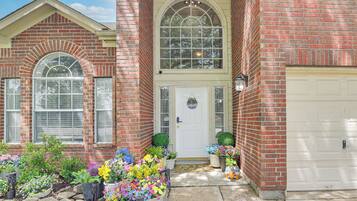A brick house with a white garage door, a front door with a wreath, and a large arched window above the door.
