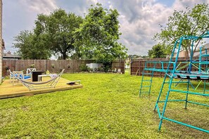 A backyard with a hammock, a trampoline, and a wooden deck.