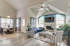 A spacious living room with a high ceiling, a dining area with a table and chairs, and a fireplace.