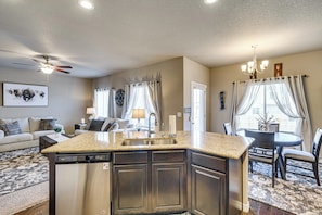 A kitchen with a central island, a dining area with a table and chairs, a ceiling fan, and a chandelier.