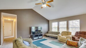 A living room with a ceiling fan, a flat-screen TV, and multiple seating options including a sofa and chairs.