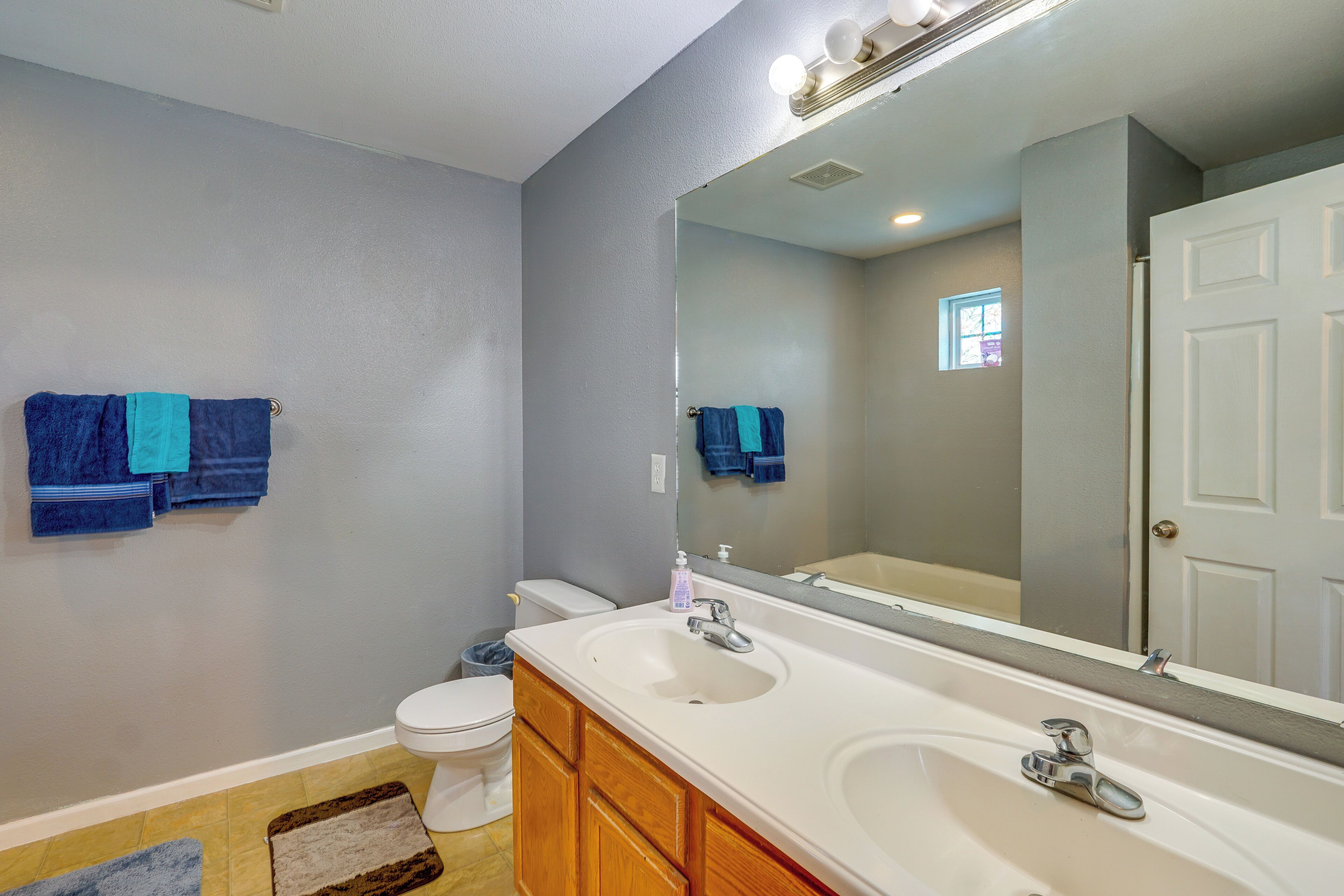 A bathroom with a white sink, wooden cabinets, a large mirror, and blue towels on the wall.