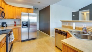 A modern kitchen with wooden cabinets, a stainless steel refrigerator, a dishwasher, and a double sink.