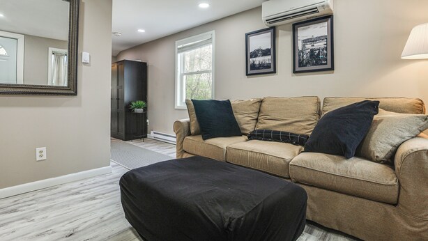 Una sala de estar con un sofá color beige, un reposapiés negro, un espejo grande y un equipo de aire acondicionado.