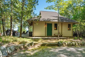 A small cabin with a green door, surrounded by trees and a gravel path.