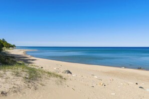A beach with clear blue water, sandy shore, and sparse vegetation.