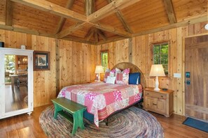 A wooden cabin bedroom with a bed, bedside tables, a bench, and a door.
