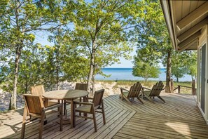 A wooden deck with a table and chairs, overlooking a beach and the ocean.