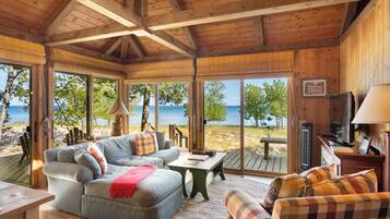 A wooden interior with a sofa, armchairs, and a table, overlooking a beach and ocean.