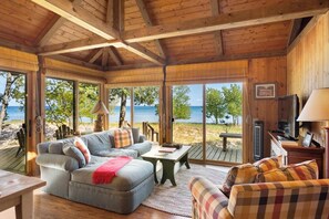 A wooden interior with a sofa, armchairs, and a table, overlooking a beach and ocean.