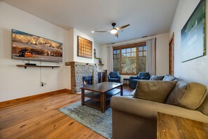 Ein Wohnzimmer mit Kamin, Deckenventilator und großen Fenstern.