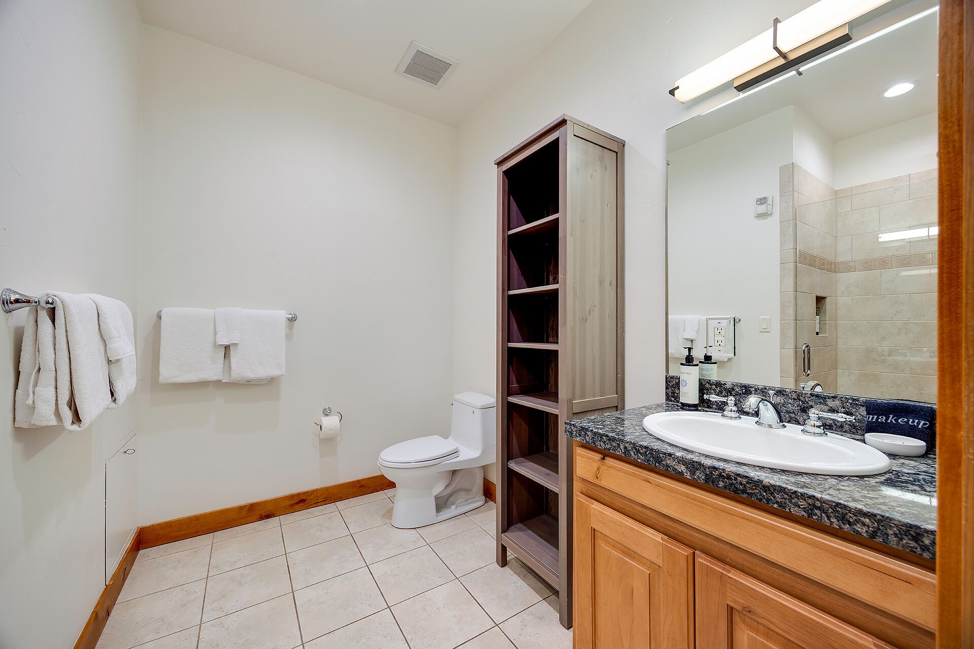 A bathroom with a toilet, a sink with a mirror, and a wooden shelf unit.