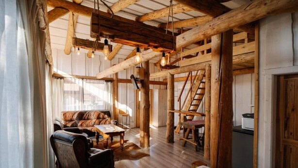 A rustic interior with exposed wooden beams, a leather sofa, a wooden dining table, and a staircase. - Gazdovsky dvor B&B Mini wellness (Bešeňová)