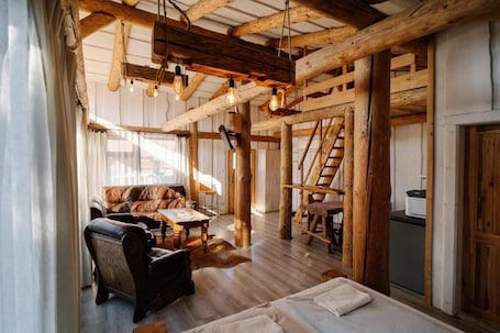 A rustic interior with exposed wooden beams, a leather sofa, a wooden dining table, and a staircase.. Gazdovsky dvor B&B Mini wellness