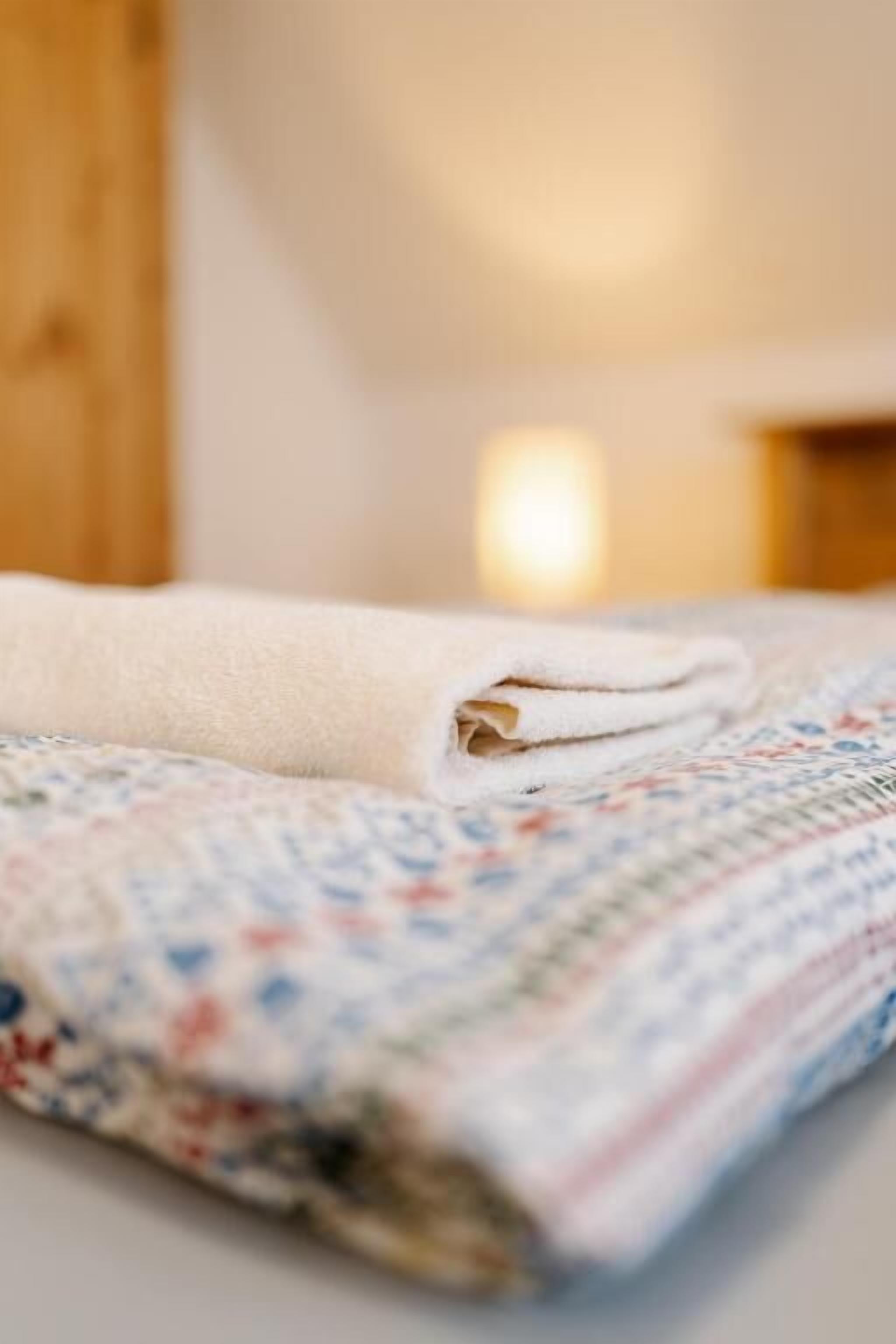 Una toalla blanca doblada cuidadosamente sobre una cama con cubrecama estampado con motivos florales.