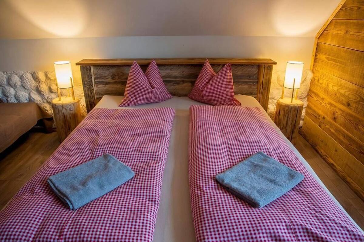 A room with two beds, each with a checkered bedspread and pillows, wooden headboard, and bedside lamps.