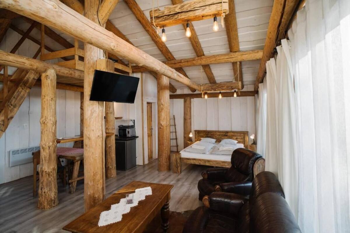 A rustic wooden room with a bed, a TV, a table, and a leather couch.