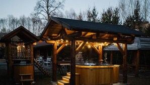 A wooden outdoor hot tub area with steps leading up to it, surrounded by a wooden deck and a covered seating area. - Gazdovsky dvor B&B Mini wellness (Bešeňová)