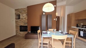 A modern dining area with a stone wall, a flat-screen TV, and a large pendant light. - Il Ginepro Oasi Montana - Appartamento moderno con 1 camera da letto (Villa Celiera)