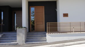 A modern building entrance with a wooden door, concrete steps, and a metal railing. - Il Ginepro Oasi Montana - Appartamento moderno con 1 camera da letto (Villa Celiera)