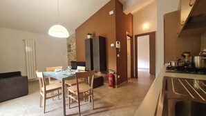 A modern kitchen with a gas stove, a dining area with a table and chairs, and a living room with a sofa. - Il Ginepro Oasi Montana - Appartamento moderno con 1 camera da letto (Villa Celiera)