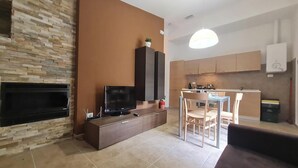 A modern living room with a fireplace, a TV, and a dining area with a table and chairs. - Il Ginepro Oasi Montana - Appartamento moderno con 1 camera da letto (Villa Celiera)