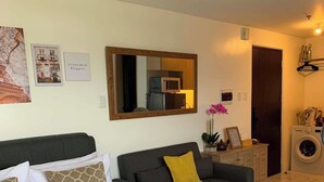 Ett hotellrum med en säng, en soffa, en spegel, en tvättmaskin och en dörr.