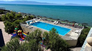 A swimming pool with a deck, surrounded by greenery, and overlooking a body of water with mountains in the distance.