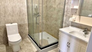 A bathroom with a glass-enclosed shower, a toilet, and a sink with a mirror above it.