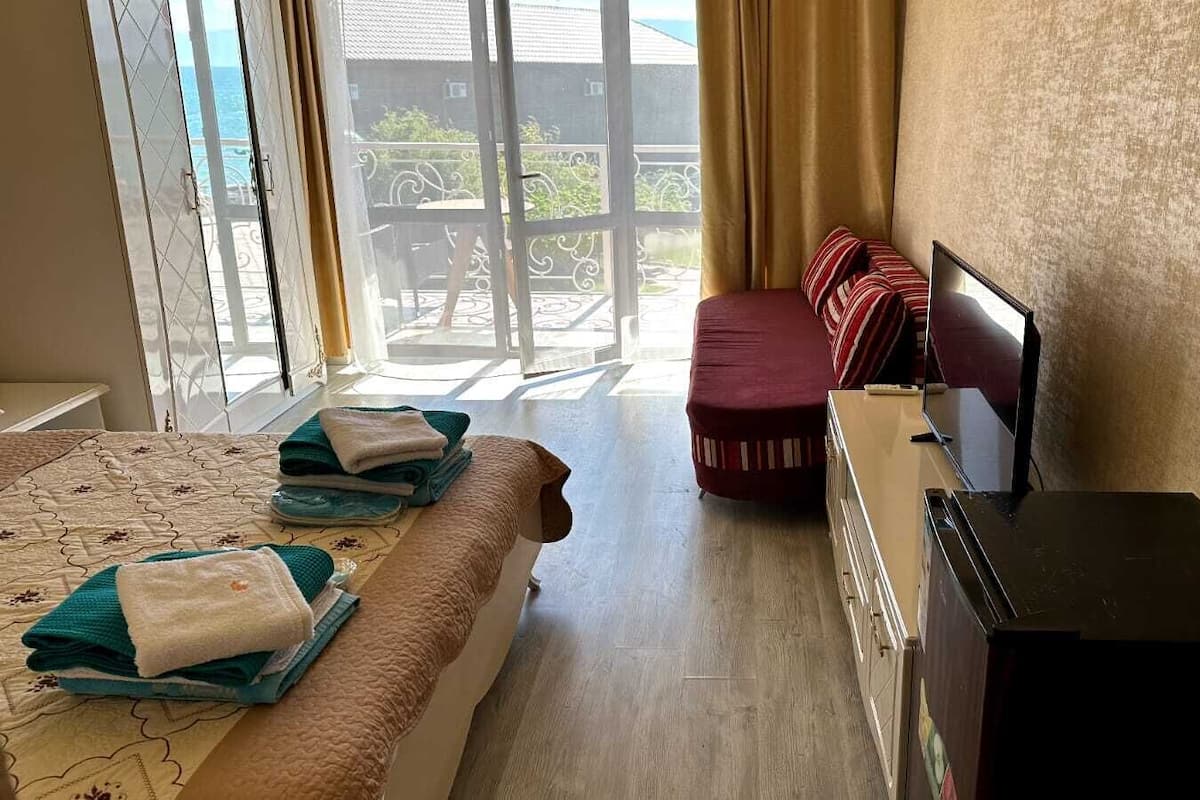 A hotel room with a bed, a desk, a chair, a TV, and a view of the outside.