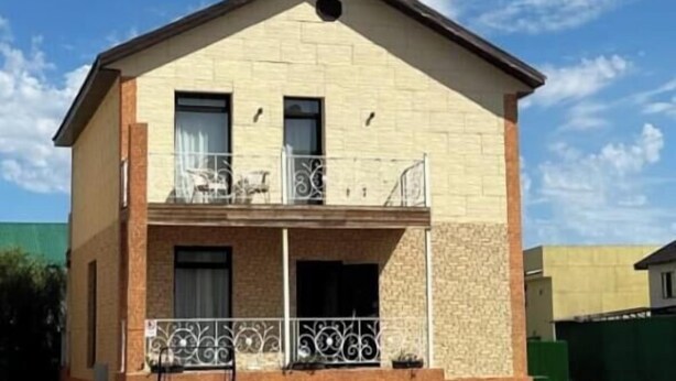 A two-story building with a balcony, a small porch, and a paved driveway.