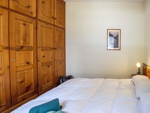 Ein Schlafzimmer mit einem Bett, einem Holzschrank, einem gerahmten Bild an der Wand und einer Nachttischlampe.