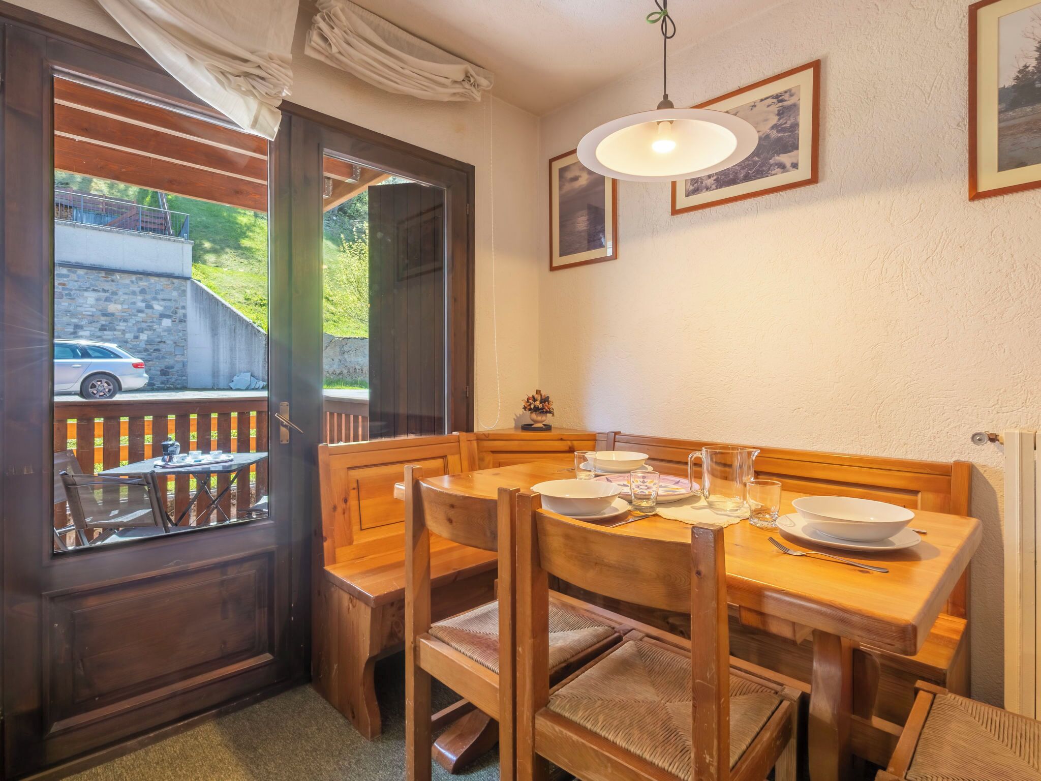 A dining area with a wooden table and benches, a window with curtains, and framed pictures on the wall.