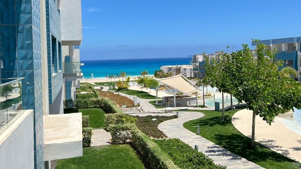 A modern hotel with a view of the ocean, featuring a landscaped garden, a pool area, and a clear sky. - Fouka North Coast SA-5A-102 (Marsa Matrouh)
