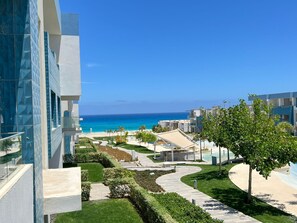 A modern hotel with a view of the ocean, featuring a landscaped garden, a pool area, and a clear sky.