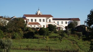 Un grand bâtiment blanc, surmonté d’un toit recouvert de tuiles rouges, entouré de verdure et d’arbres.
