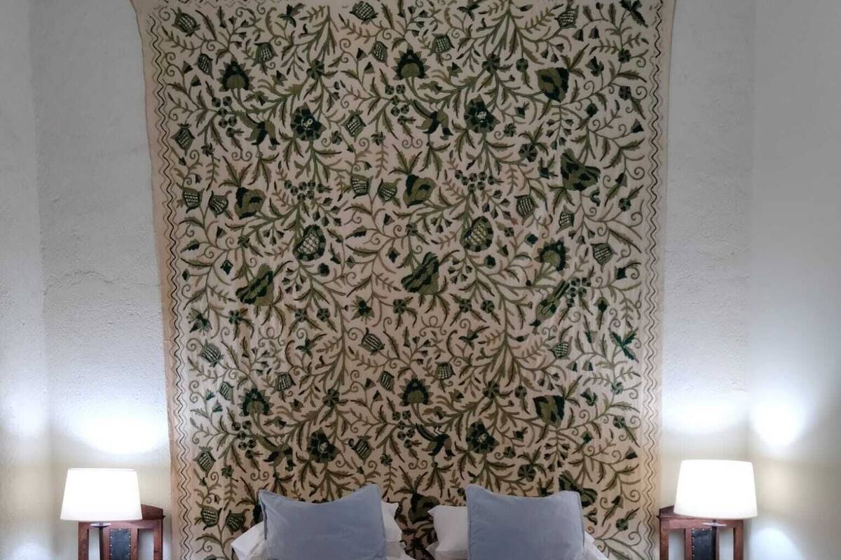 A bed with a patterned tapestry headboard, two bedside lamps, and a white bedspread.