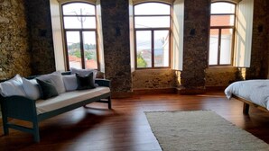 Une pièce avec un mur en pierre, un plancher en bois, un lit, un canapé et deux fenêtres avec des rideaux.