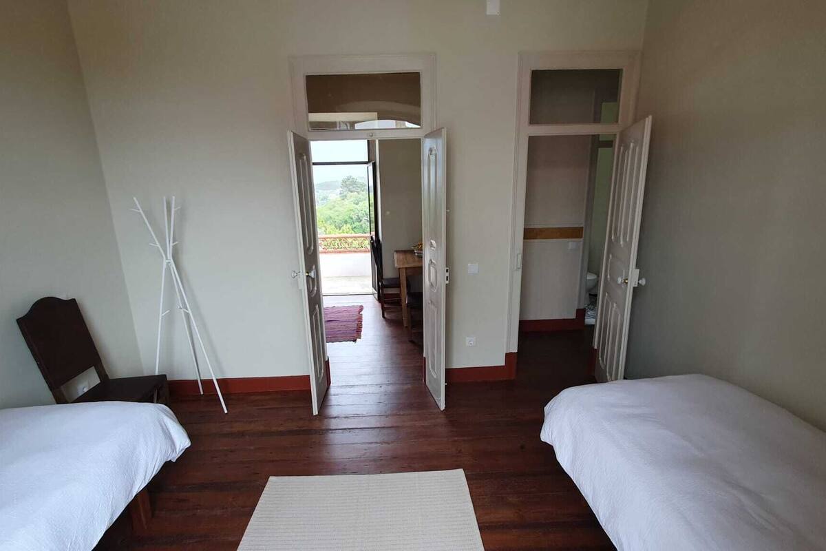 A room with two beds, a coat rack, and a view through an open door to a balcony.