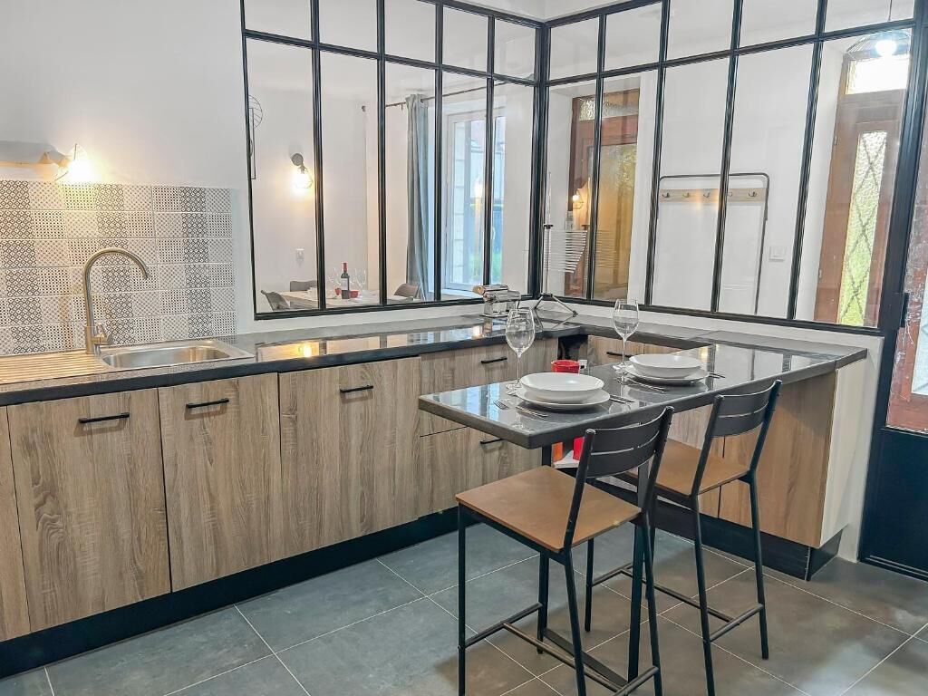 A modern kitchen with a central island, bar stools, and a view through large windows.