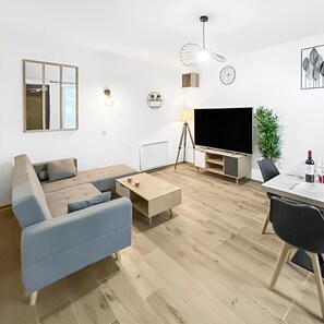 A modern living room with a sofa, coffee table, TV, and a dining area with chairs and a table. - Bright house with glass roof & large screen (Saint-Leu-d'Esserent)