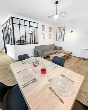 A modern dining area with a wooden table set for six, a grey sofa, and a glass partition wall. - Bright house with glass roof & large screen (Saint-Leu-d'Esserent)